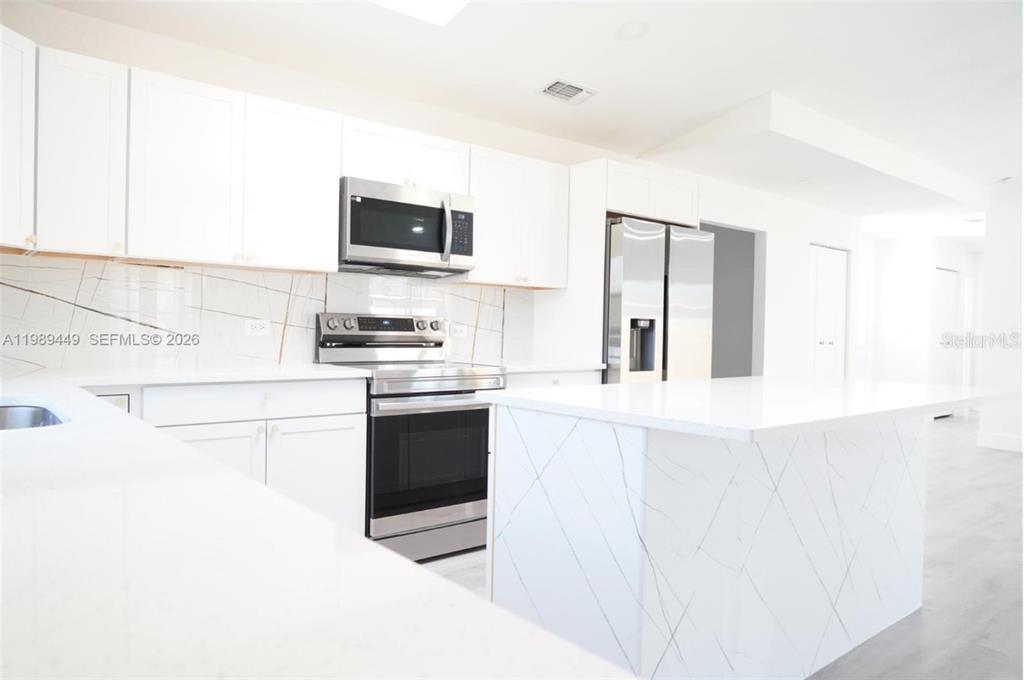 A modern kitchen features white cabinets, stainless steel appliances, and a marble-patterned island — 563 PRESQUE ISLE DRIVE, PORT CHARLOTTE, FL
