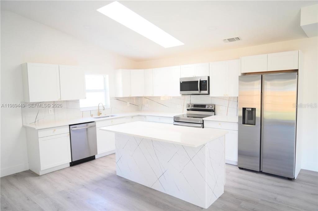 A modern kitchen features white cabinets, a marble-patterned island, and stainless steel appliances — 563 PRESQUE ISLE DRIVE, PORT CHARLOTTE, FL