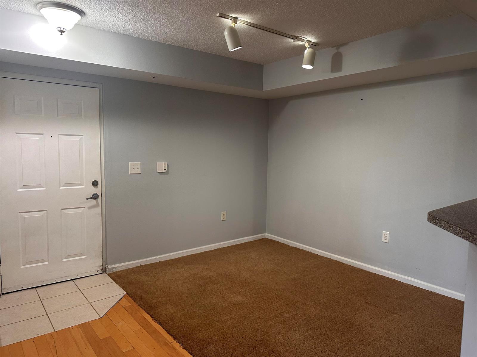 An empty room features gray walls, brown carpeting, a white door, and track lighting — 3628 NW Adriatic Lane, Jensen Beach FL 34957, JENSEN BEACH, FL