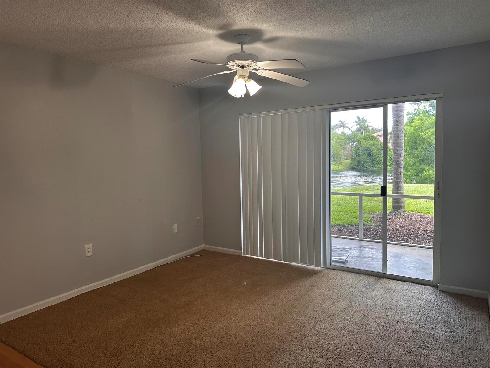 An empty room with tan carpet, gray walls, a ceiling fan, and sliding glass doors — 3628 NW Adriatic Lane, Jensen Beach FL 34957, JENSEN BEACH, FL