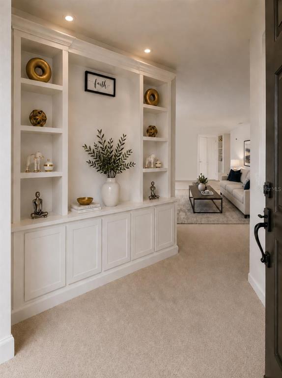A white built-in shelving unit with decor stands in a carpeted entryway near a living room — 4592 BIG ISLAND DRIVE, KISSIMMEE, FL