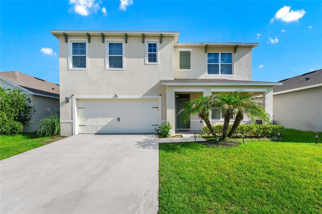 A two-story suburban house with a beige stucco exterior, a two-car garage, and a palm tree — 529 TALISI LOOP, ST CLOUD, FL