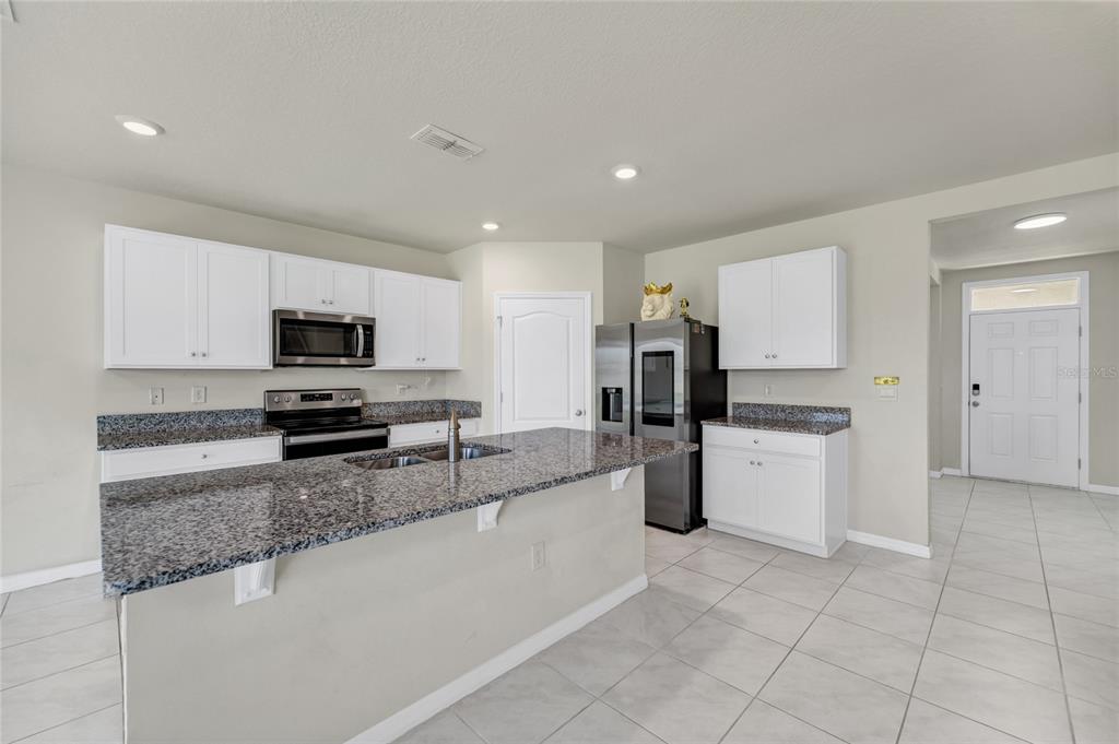 A kitchen with white cabinets, granite countertops, a center island, and stainless steel appliances — 529 TALISI LOOP, ST CLOUD, FL