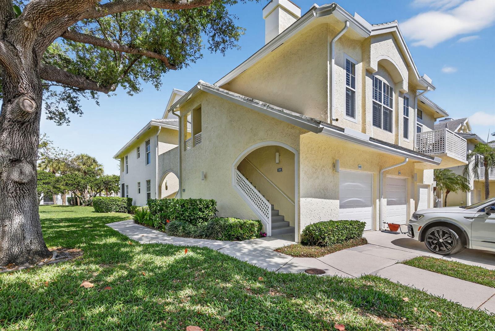 A yellow two-story townhouse with a garage, exterior staircase, and a large tree nearby — 1403 Mainsail Circle, Jupiter FL 33477, JUPITER, FL
