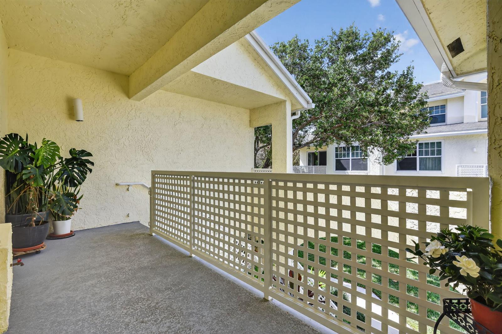 A covered balcony features a light-colored lattice railing, concrete flooring, and potted plants — 1403 Mainsail Circle, Jupiter FL 33477, JUPITER, FL