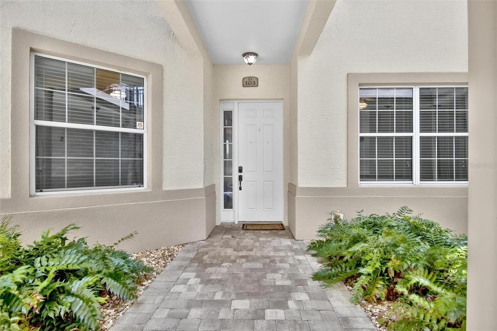 A paved walkway leads to the white front door of a residential building unit — 200 RIVERFRONT DRIVE UNIT D103, PALM COAST, FL
