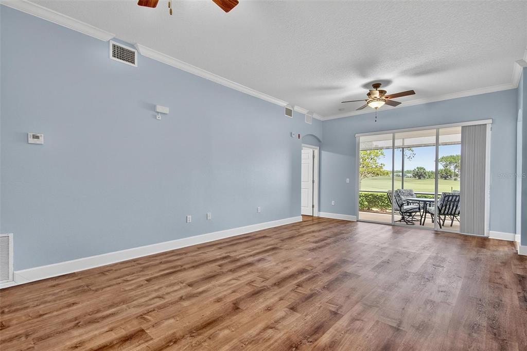 A spacious living room with light blue walls, wood-look flooring, and sliding glass patio doors — 200 RIVERFRONT DRIVE UNIT D103, PALM COAST, FL