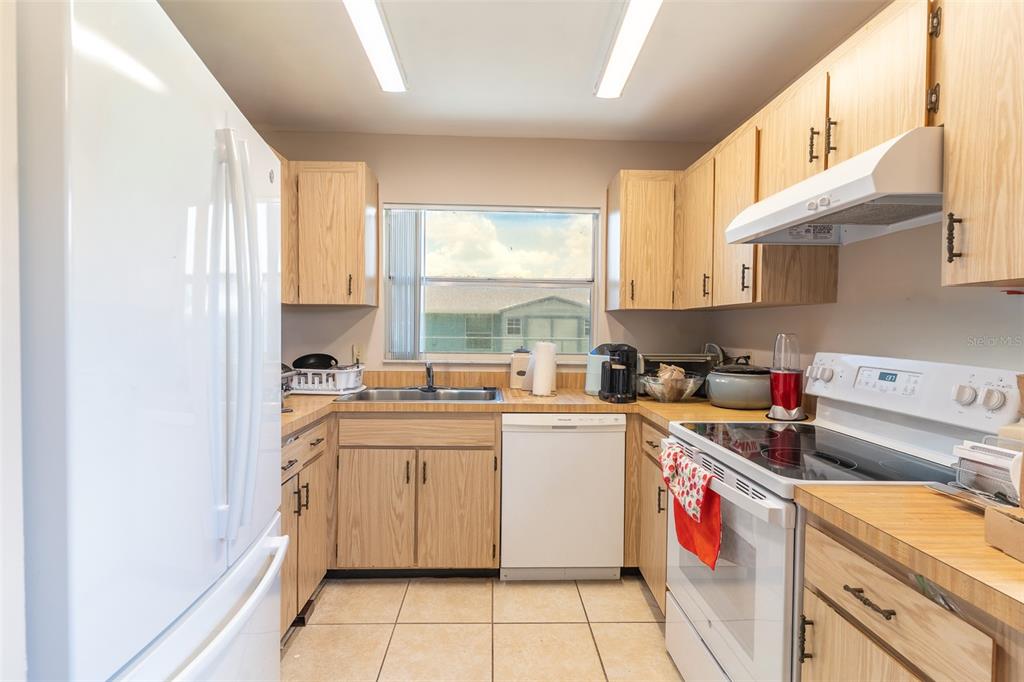 A kitchen features light wood cabinets, laminate countertops, white appliances, and tiled flooring — 443 BALL COURT, KISSIMMEE, FL