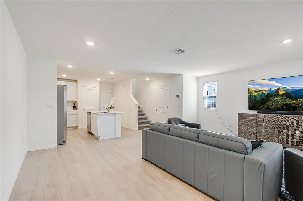 An open-concept living room and kitchen featuring light wood flooring, white cabinetry, and a staircase — 4355 HAZEL STREET, KISSIMMEE, FL