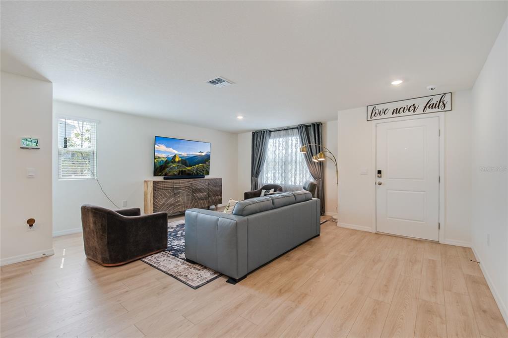 A living room features light wood flooring, a gray sofa, a television, and an entryway — 4355 HAZEL STREET, KISSIMMEE, FL