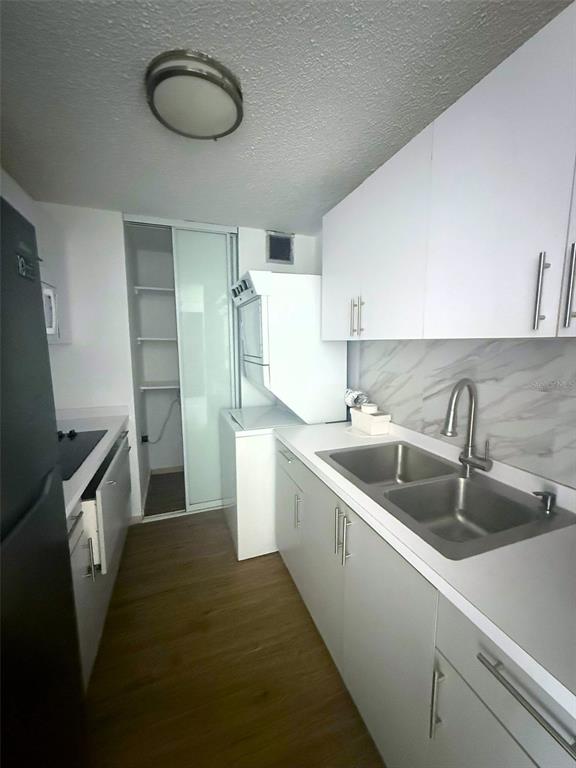 A galley kitchen features white cabinets, a double sink, and a stacked washer and dryer — 3 CALLE HORTENSIA UNIT 17E, SAN JUAN, PR