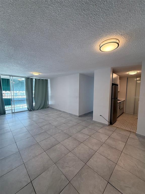 An open living area with light tile flooring leads to a kitchen and balcony — 3 CALLE HORTENSIA UNIT 17E, SAN JUAN, PR