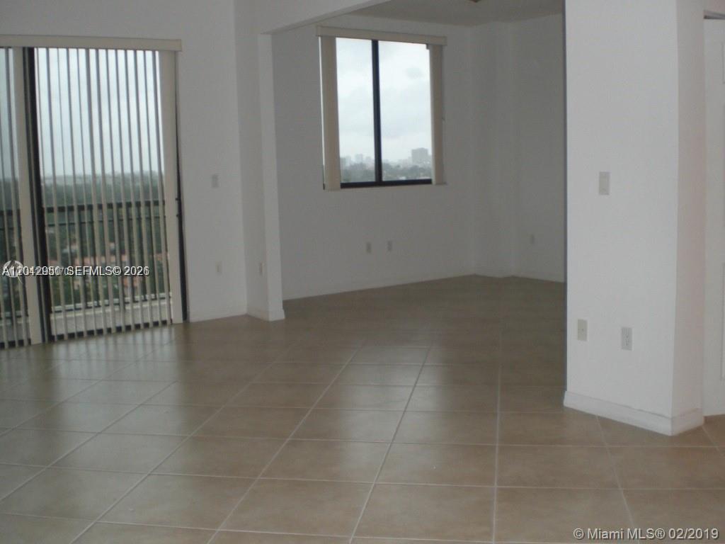 An empty room features beige tile flooring, white walls, vertical blinds, and a window view — 3590 CORAL WAY # 902, Miami FL 33145, MIAMI, FL