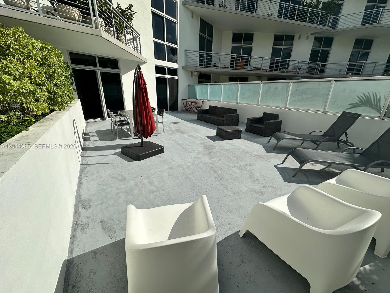 A spacious outdoor patio features lounge chairs, patio furniture, and a red umbrella — 2001 Meridian Ave # 309, Miami Beach FL 33139, MIAMI BEACH, FL