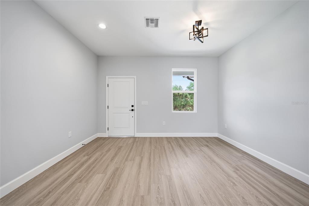 An empty room features light gray walls, wood-look flooring, a white door, and a window — 13443 KAPLAN TERRACE, PORT CHARLOTTE, FL
