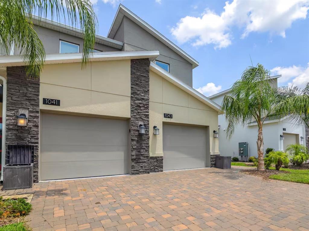 A two-story duplex with beige stucco walls, stone accents, and two gray garage doors — 1043 SPLASH SHOT PLACE UNIT 2002, DAVENPORT, FL