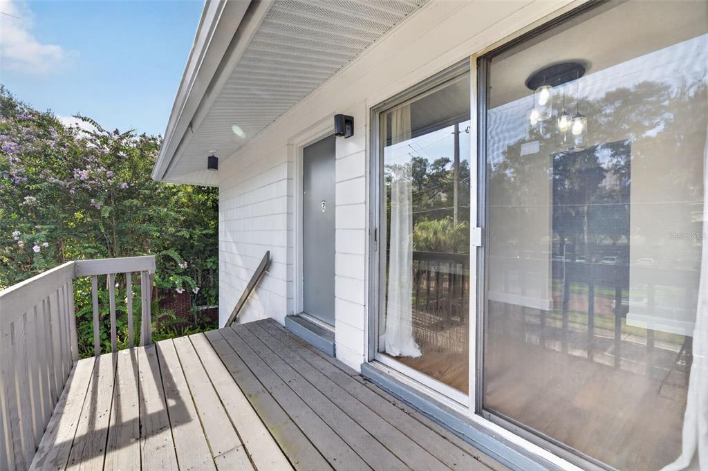 A wooden balcony with a gray door and sliding glass doors on a white building — 118 W AMERICA STREET UNIT 2, ORLANDO, FL