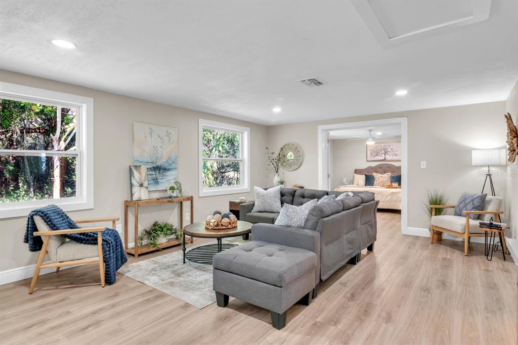 A living room features a grey sectional sofa, wood-look flooring, and an adjacent bedroom doorway — 11416 PINE FOREST DRIVE, NEW PORT RICHEY, FL
