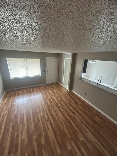 An empty room features wood-look flooring, a popcorn ceiling, and a kitchen pass-through window — 4403 PRAIRIE COURT UNIT B, ORLANDO, FL