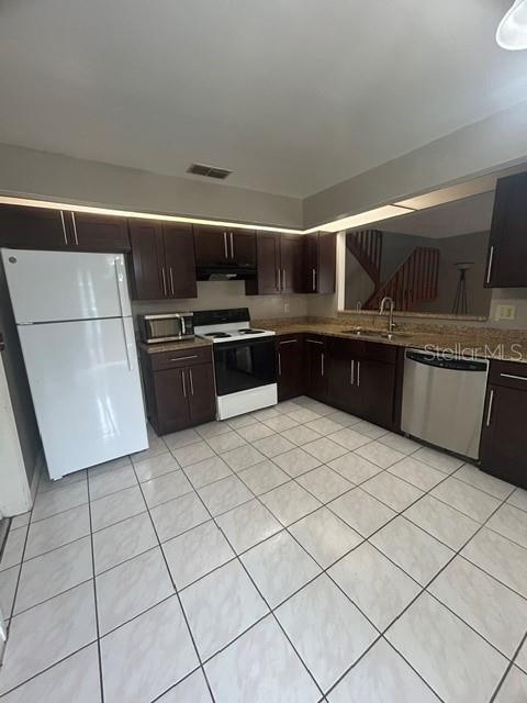A kitchen features dark wood cabinets, white appliances, and light-colored tiled flooring — 4403 PRAIRIE COURT UNIT B, ORLANDO, FL
