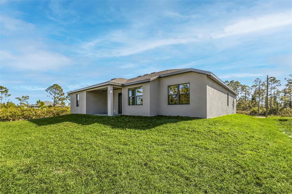 The rear exterior of a single-story house features a covered patio and a grassy yard — 5227 DAYTON LANE, PORT CHARLOTTE, FL
