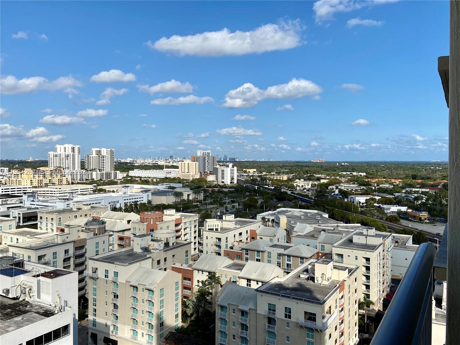 An elevated view of a suburban cityscape featuring apartment buildings, a shopping center, and distant skyscrapers — 9055 SW 73rd Ct # 1709, Miami FL 33156, MIAMI, FL
