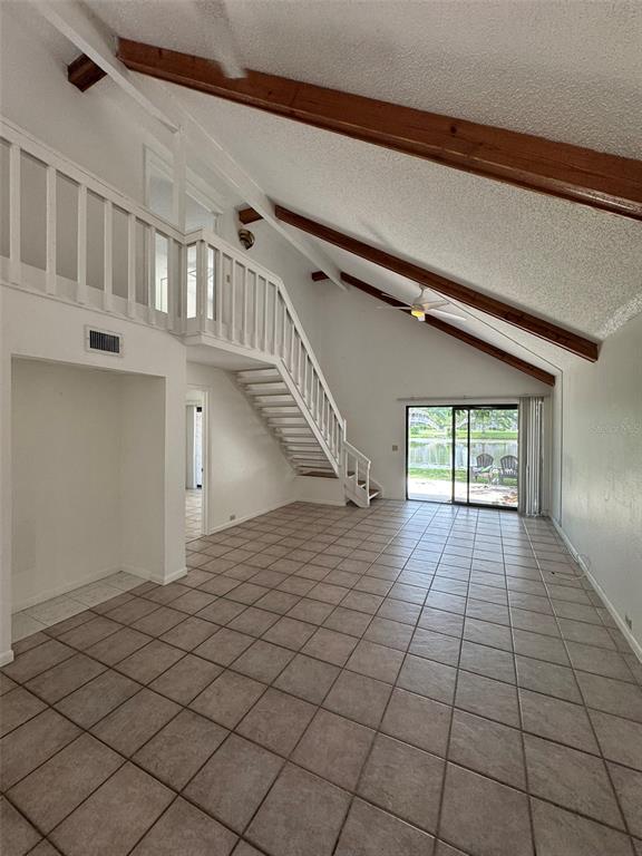 A living room with a vaulted ceiling, exposed wooden beams, a staircase, and sliding glass doors — 4009 MURIEL PLACE, TAMPA, FL