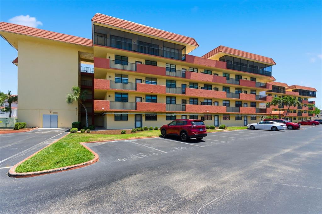 A multi-story apartment building with red-tiled roofs and a parking lot in the foreground — 19701 GULF BOULEVARD UNIT 417, INDIAN SHORES, FL