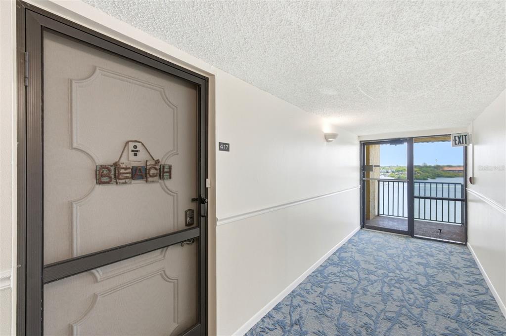 A hallway with a door labeled "Beach," blue patterned carpet, and a view of water — 19701 GULF BOULEVARD UNIT 417, INDIAN SHORES, FL
