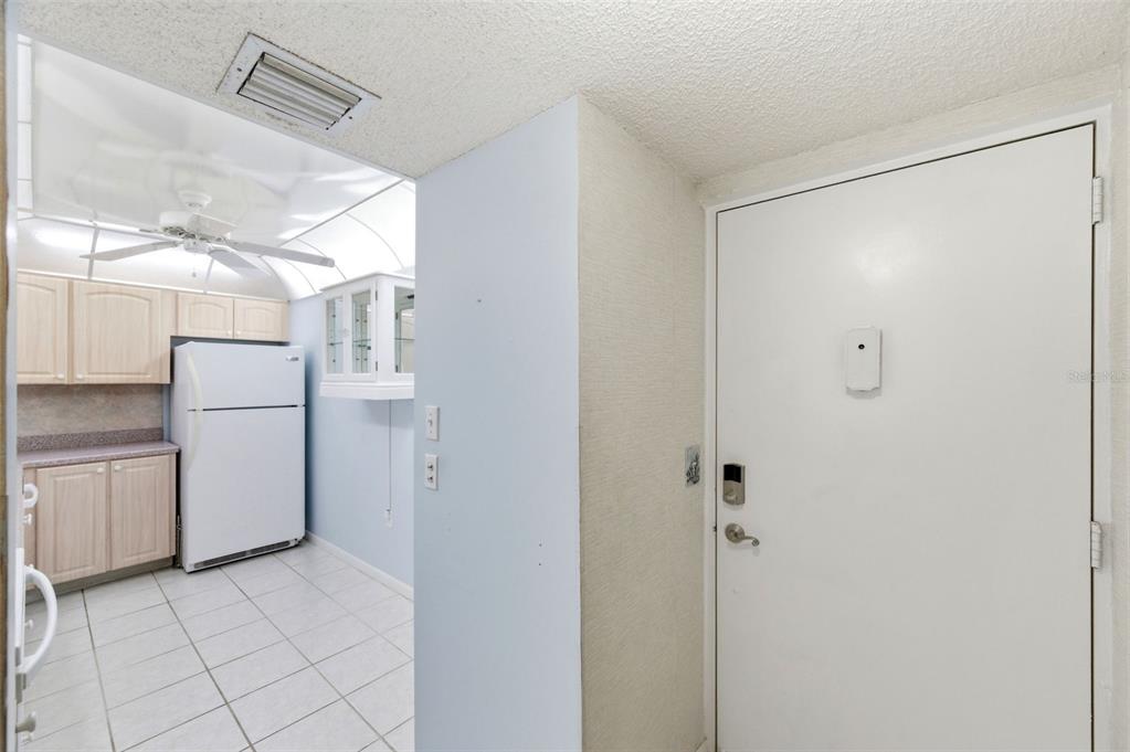 A white entry door stands next to a kitchen with light wood cabinets and tile flooring — 19701 GULF BOULEVARD UNIT 417, INDIAN SHORES, FL