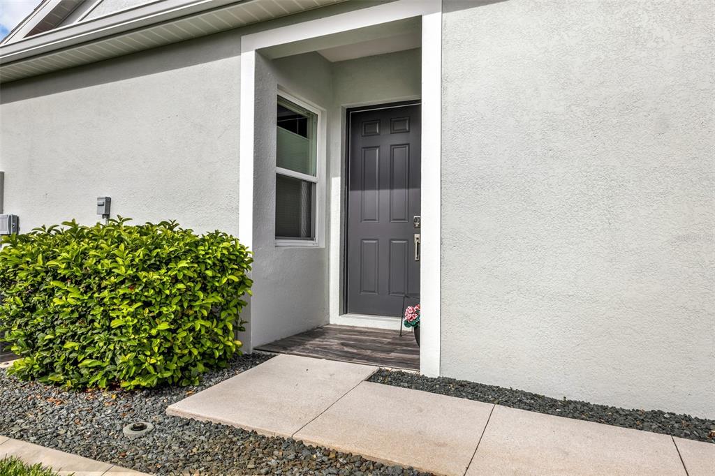 A gray front door is set within a white stucco entryway next to a green bush — 24343 WESTGATE BOULEVARD, PUNTA GORDA, FL