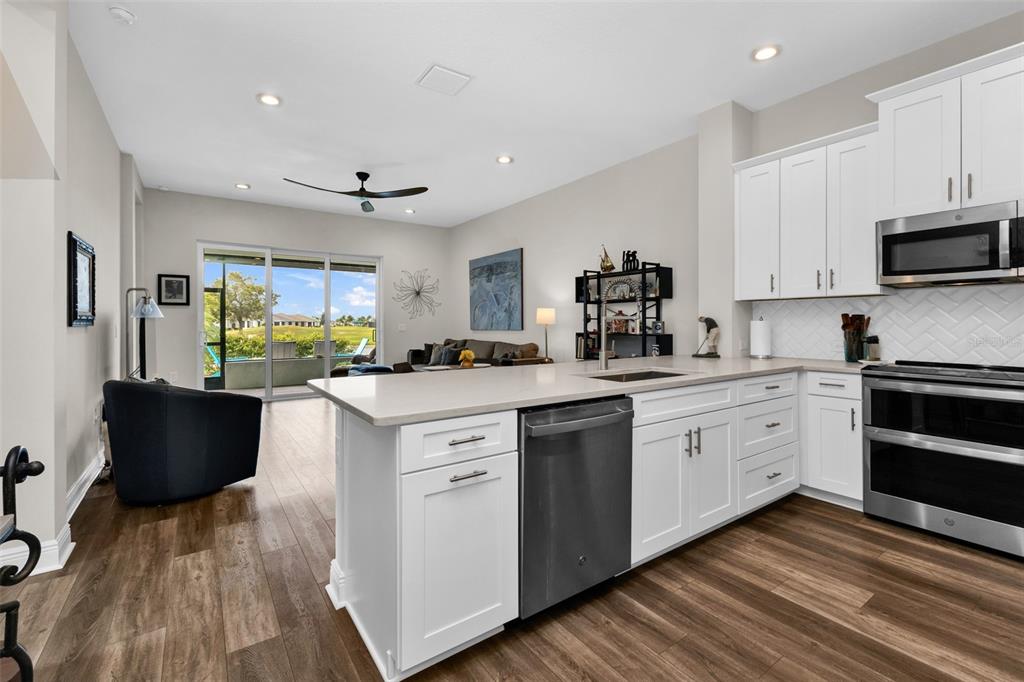 A modern kitchen with white cabinets and stainless steel appliances opens to a living area — 24343 WESTGATE BOULEVARD, PUNTA GORDA, FL