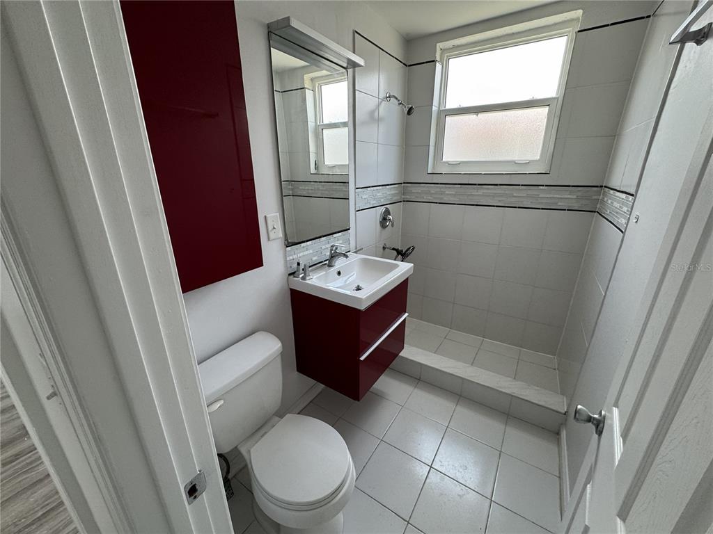 A bathroom features a red vanity, a white toilet, and a tiled walk-in shower — 428 ARMADA ROAD S UNIT 6, VENICE, FL