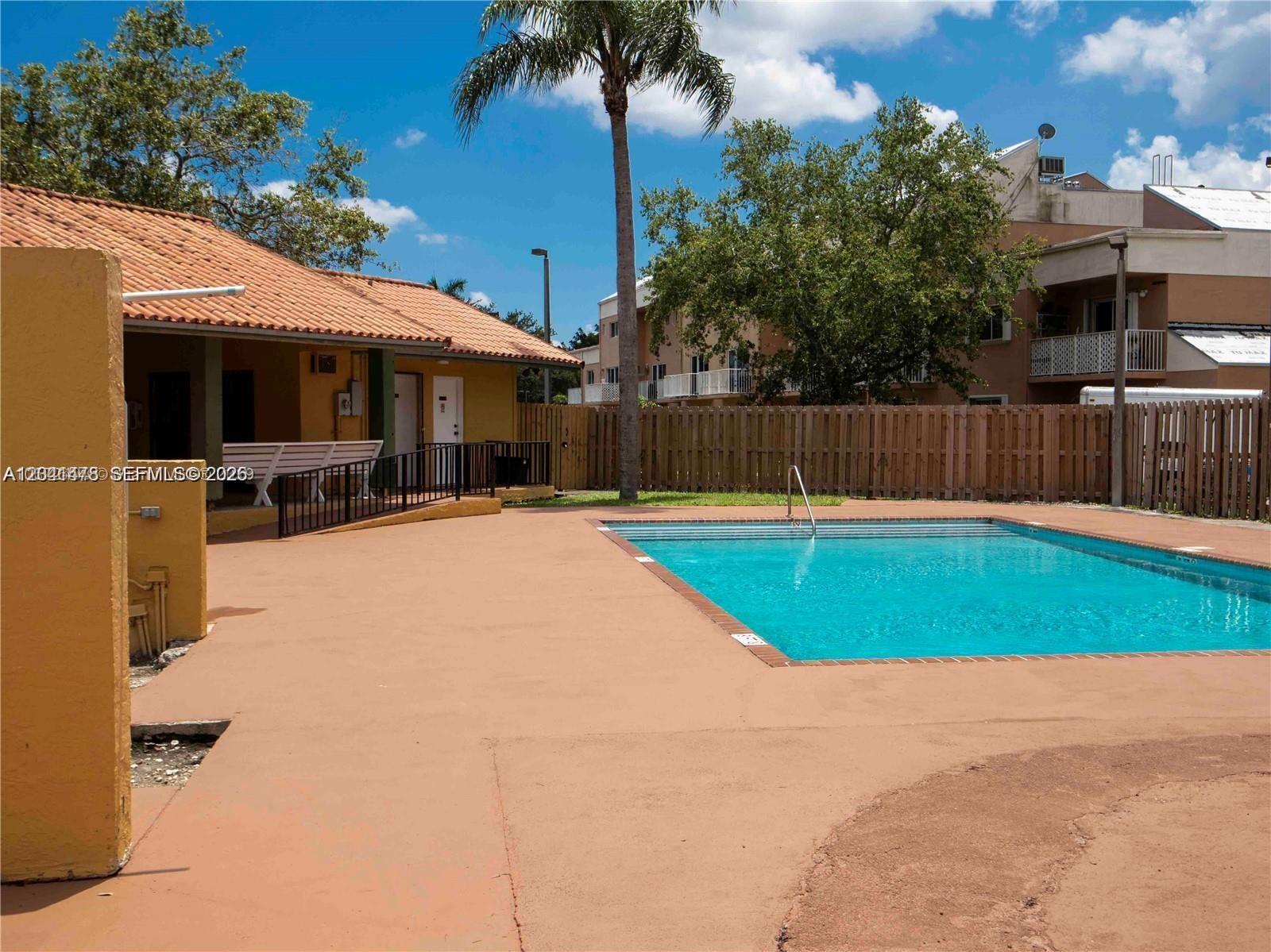 A swimming pool sits on a concrete deck next to a building with a porch — 14831 SW 80th St # 4, Miami FL 33193, MIAMI, FL