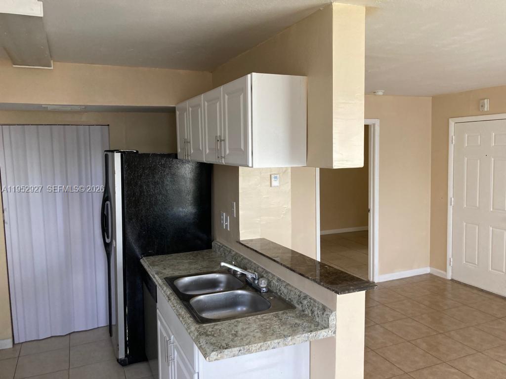 A kitchen features white cabinets, a dark countertop, a double sink, and a black refrigerator — 8705 NW 39th St # 0, Sunrise FL 33351, SUNRISE, FL