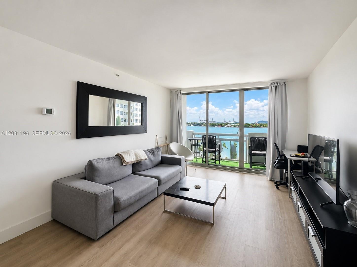 A living room features a gray sofa, coffee table, and sliding glass doors overlooking water — 1500 Bay Rd # 718S, Miami Beach FL 33139, MIAMI BEACH, FL