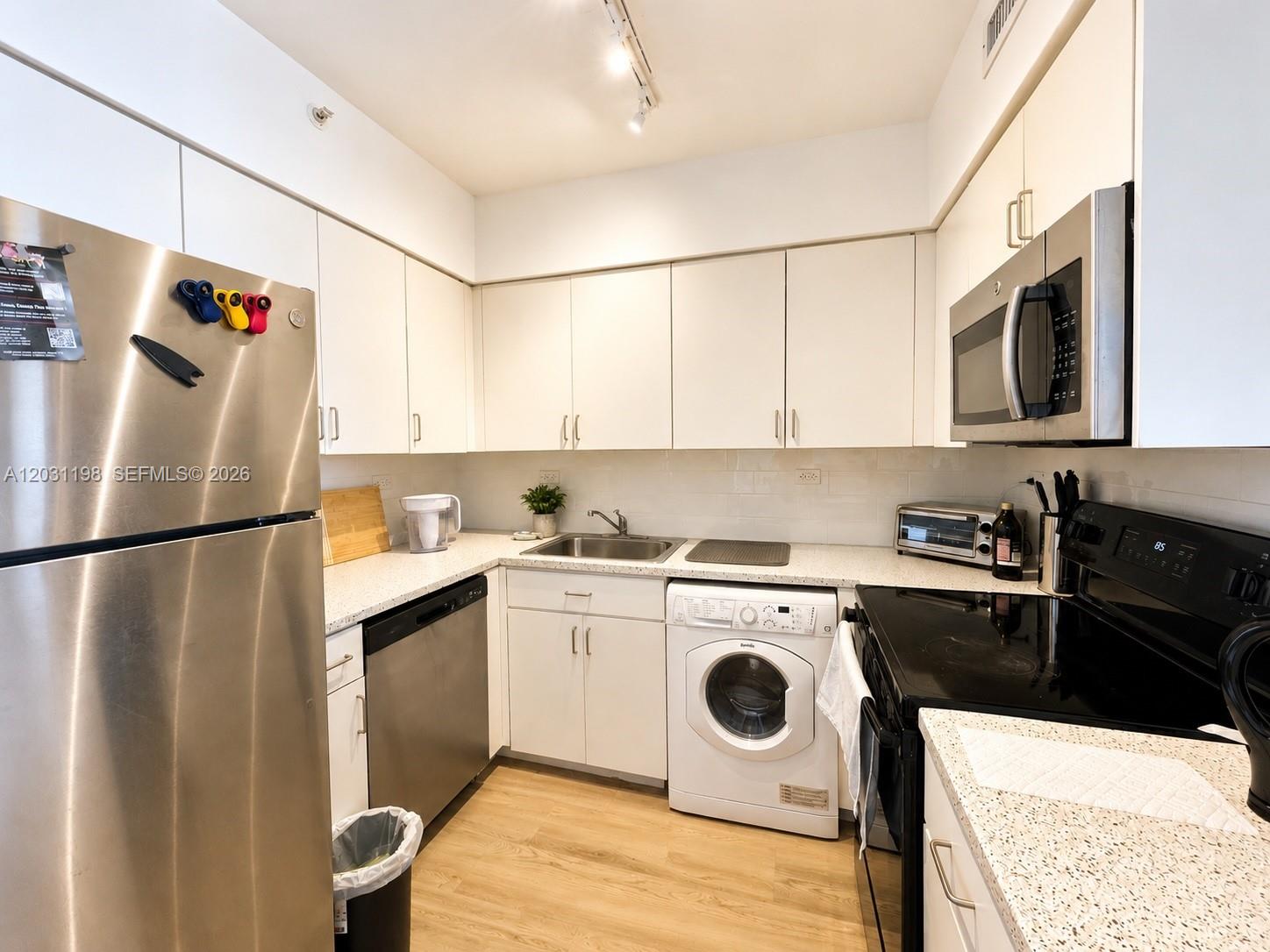 A kitchen features white cabinetry, stainless steel appliances, a built-in washer, and speckled countertops — 1500 Bay Rd # 718S, Miami Beach FL 33139, MIAMI BEACH, FL