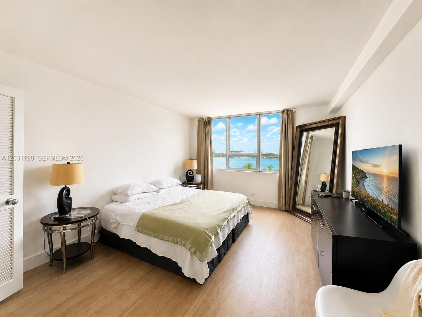 A bedroom features a bed, a dresser with a television, and a large floor mirror — 1500 Bay Rd # 718S, Miami Beach FL 33139, MIAMI BEACH, FL