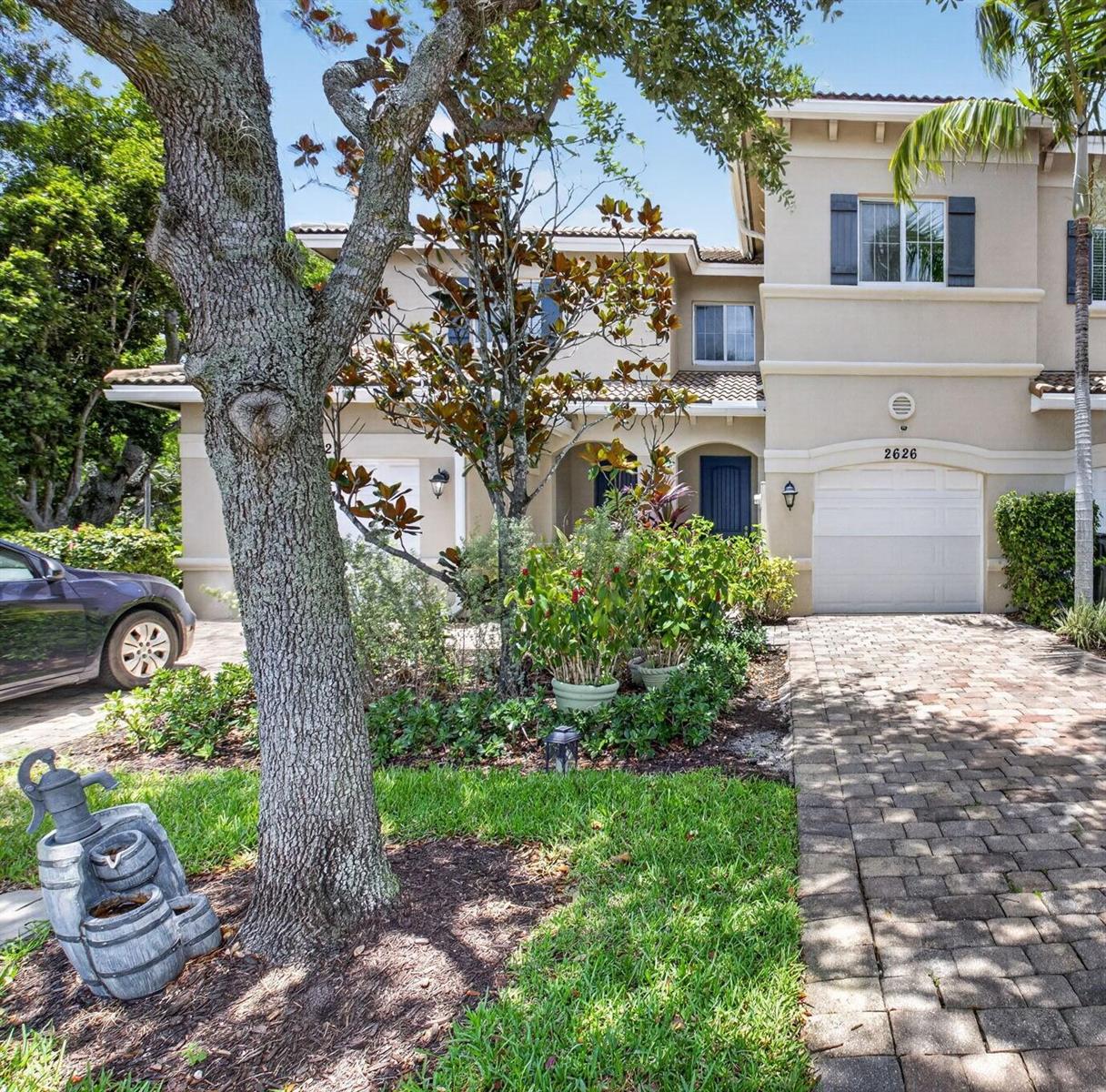 A two-story stucco townhouse features a brick driveway, a garage, and a large front tree — 2626 Webb Avenue, Delray Beach FL 33444, DELRAY BEACH, FL