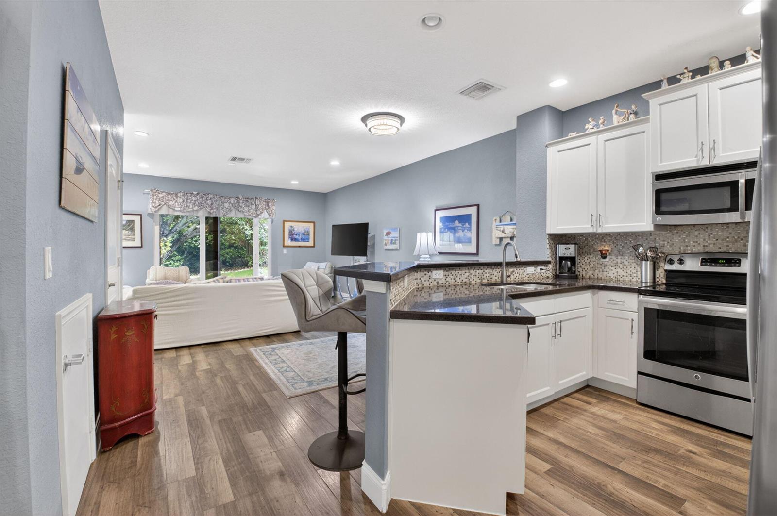 A kitchen with white cabinets and dark countertops opens into a living area with wood-look flooring — 2626 Webb Avenue, Delray Beach FL 33444, DELRAY BEACH, FL
