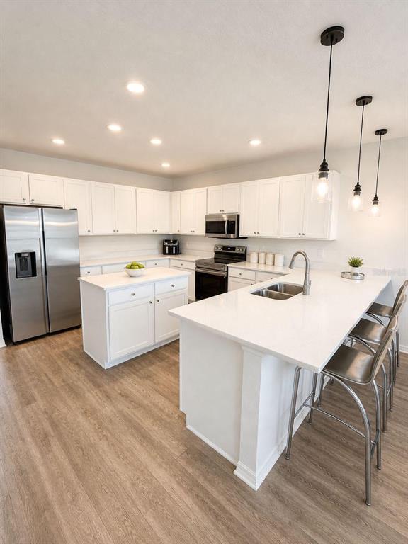 A modern kitchen features white cabinetry, stainless steel appliances, a center island, and pendant lighting — 1032 SILAS STREET, HAINES CITY, FL