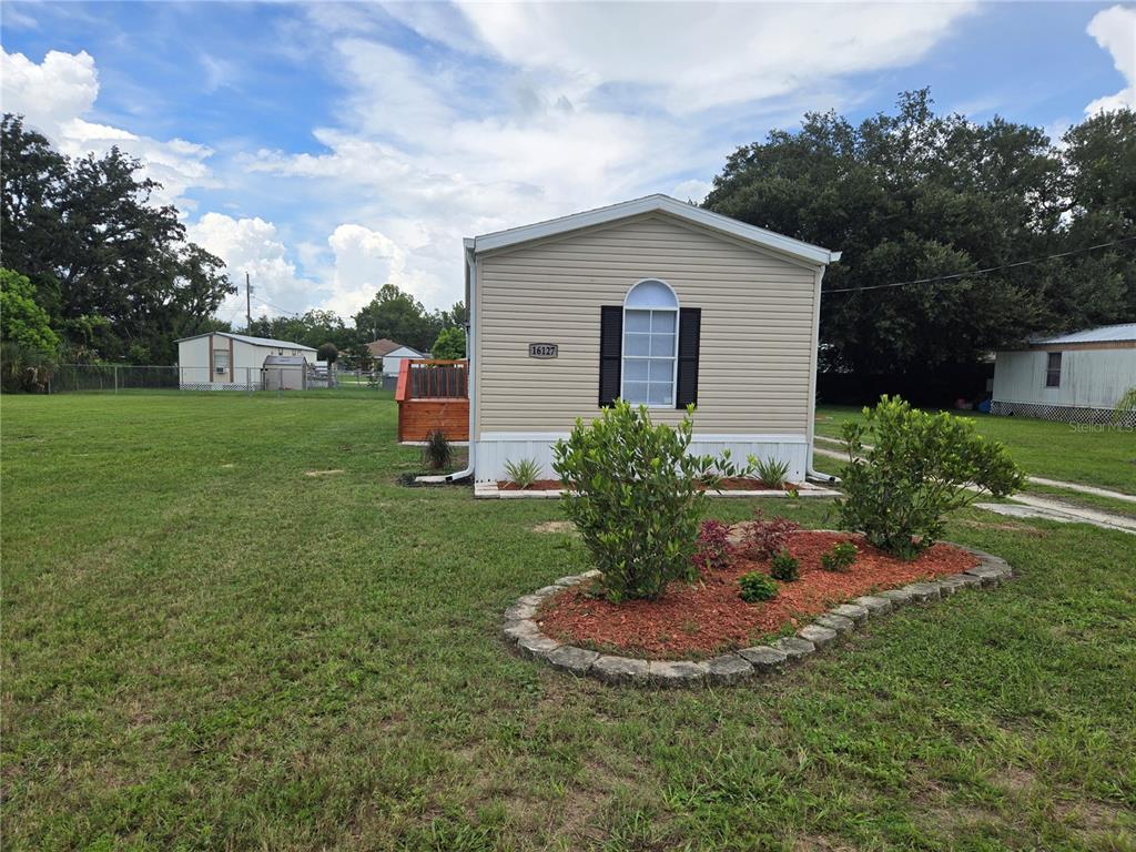 A single-story manufactured home with beige siding sits on a large, grassy lot — 16127 NARROW STREET, BROOKSVILLE, FL