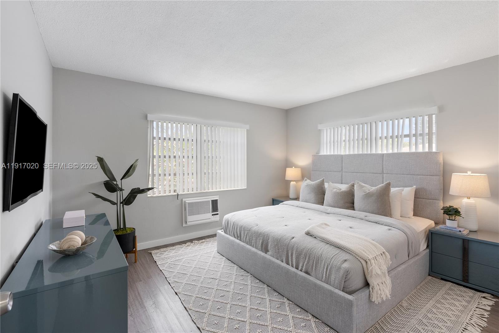 A bedroom features a gray upholstered bed, matching nightstands, a television, and a window air conditioner — 550 NE 20th St # 6, Wilton Manors FL 33305, WILTON MANORS, FL
