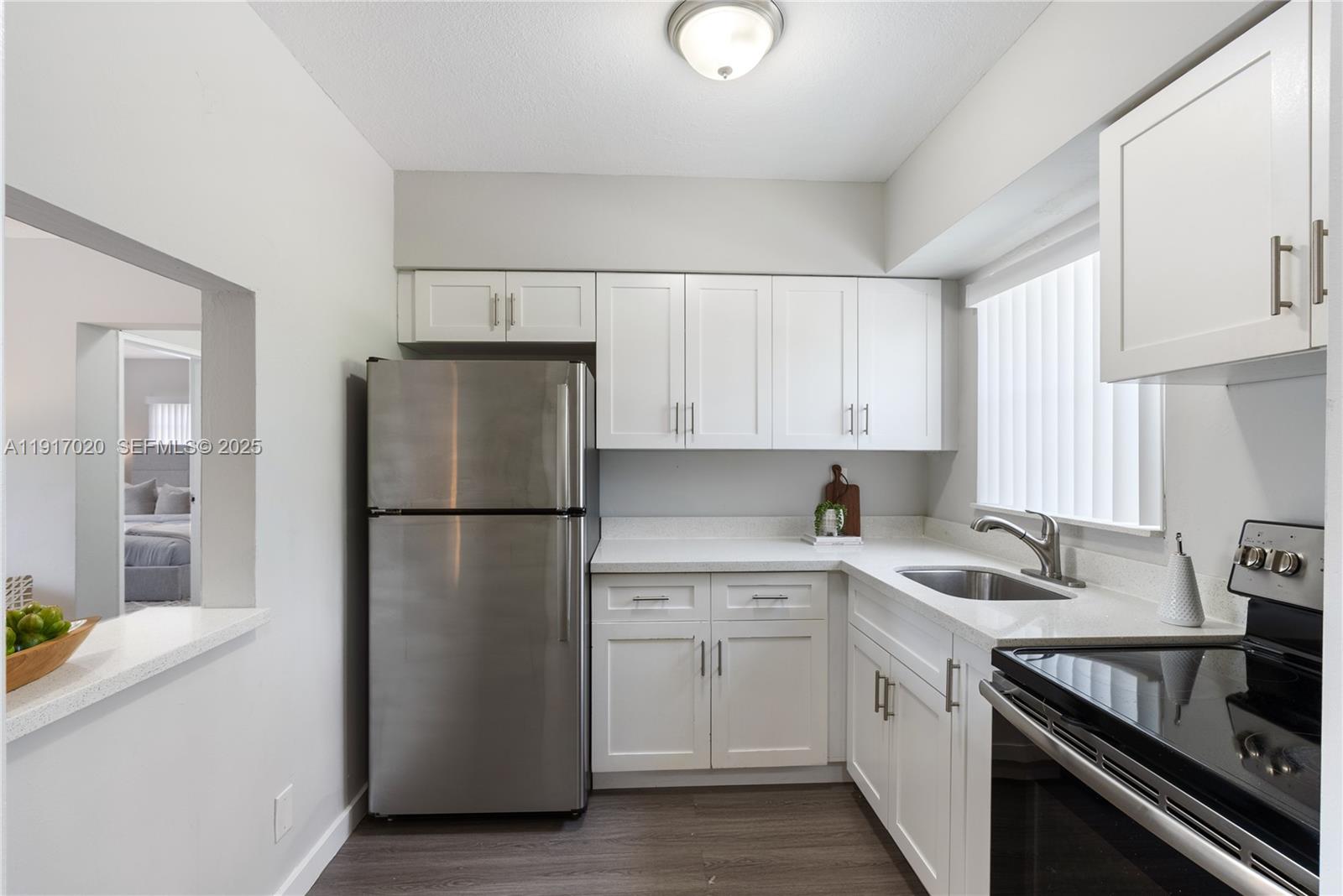 A kitchen features white cabinets, stainless steel appliances, and light countertops over dark flooring — 550 NE 20th St # 6, Wilton Manors FL 33305, WILTON MANORS, FL