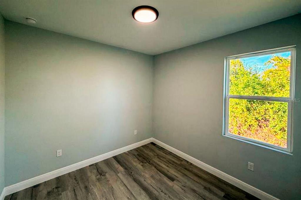 An empty bedroom features light blue walls, wood-look flooring, and a single window — 2006 E 6TH STREET, LEHIGH ACRES, FL