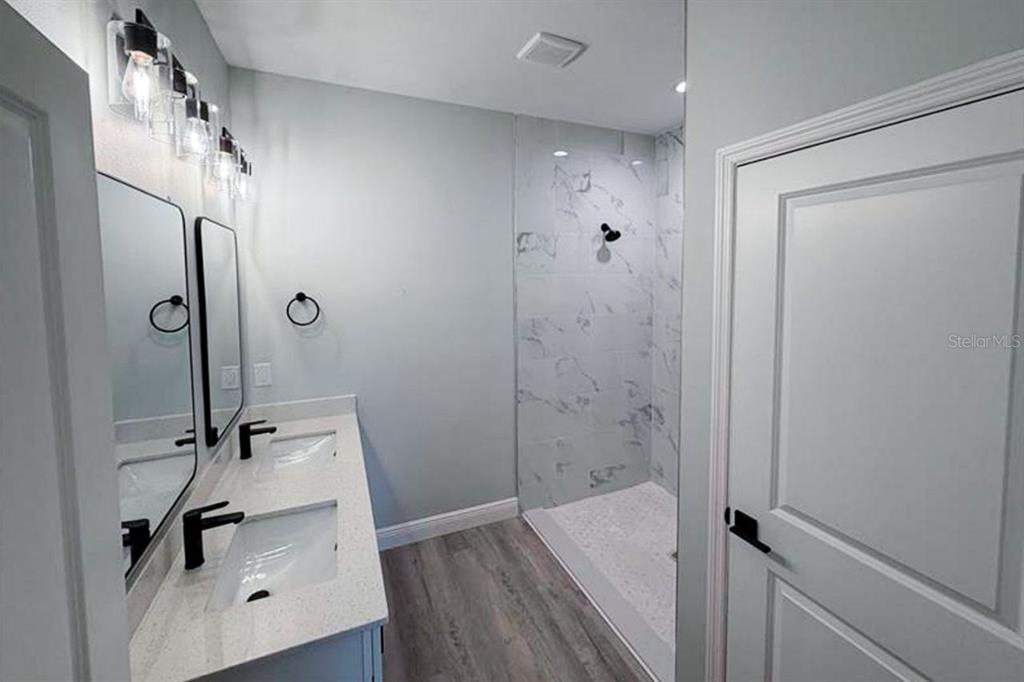 A modern bathroom features a double vanity with quartz countertops and a walk-in tile shower — 2006 E 6TH STREET, LEHIGH ACRES, FL