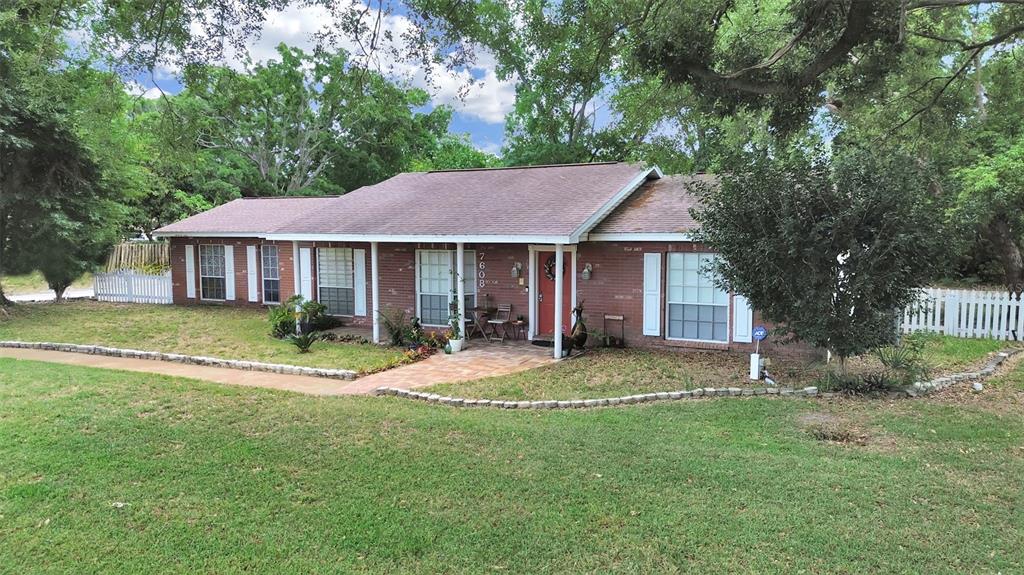 A single-story brick house with a red front door and white shutters sits on grass — 7608 BARRY ROAD, TAMPA, FL