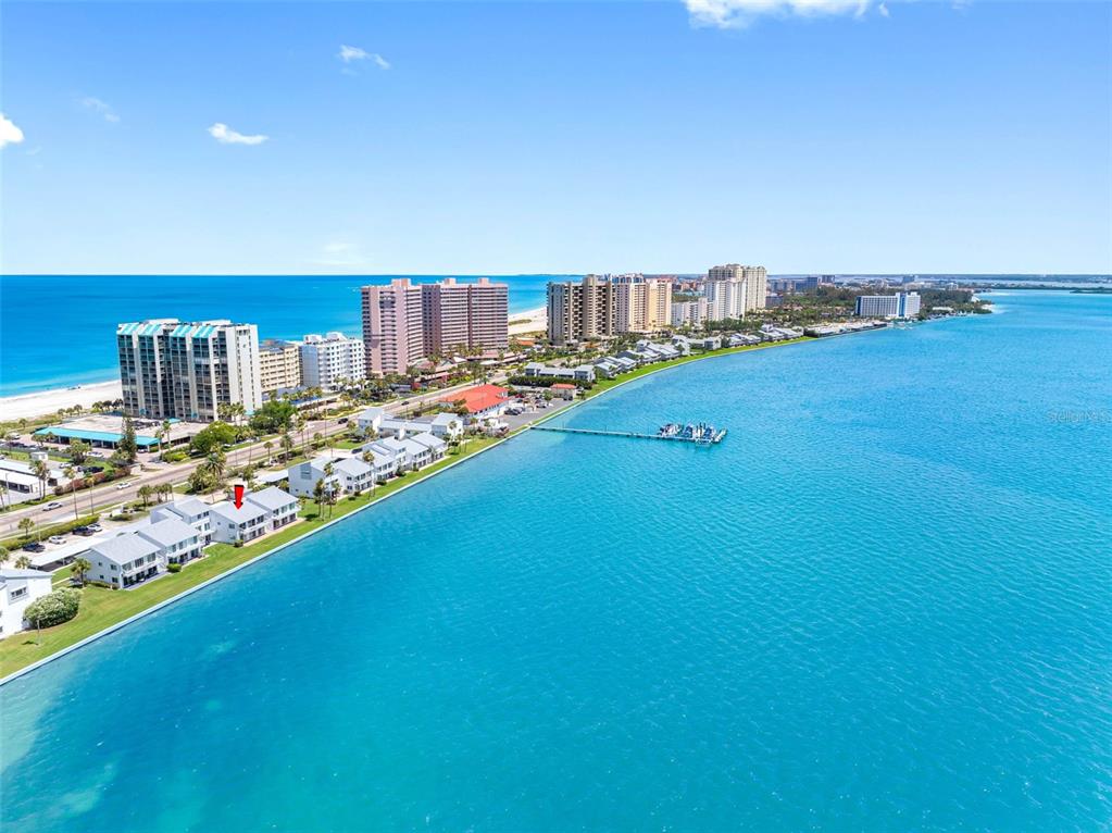 An aerial view shows a waterfront residential complex with a red arrow pointing to a building — 1401 GULF BOULEVARD UNIT 212, CLEARWATER BEACH, FL