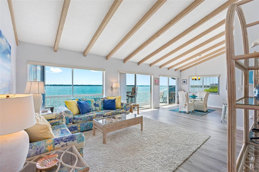 A living and dining area features vaulted beamed ceilings, light wood flooring, and water views — 1401 GULF BOULEVARD UNIT 212, CLEARWATER BEACH, FL