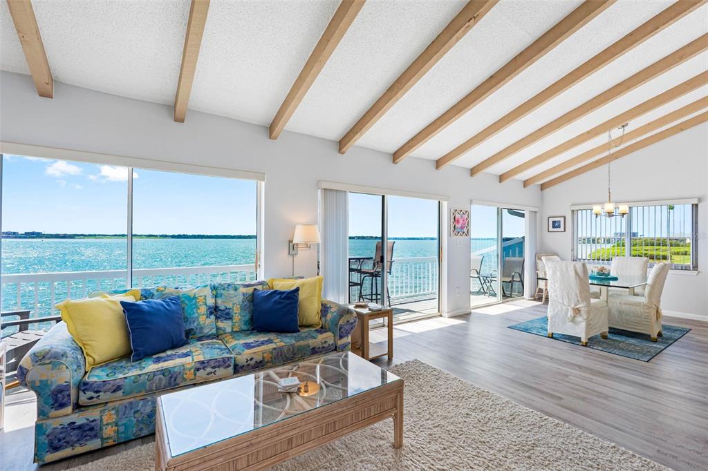 A living and dining area features vaulted wood-beam ceilings and large windows overlooking the water — 1401 GULF BOULEVARD UNIT 212, CLEARWATER BEACH, FL